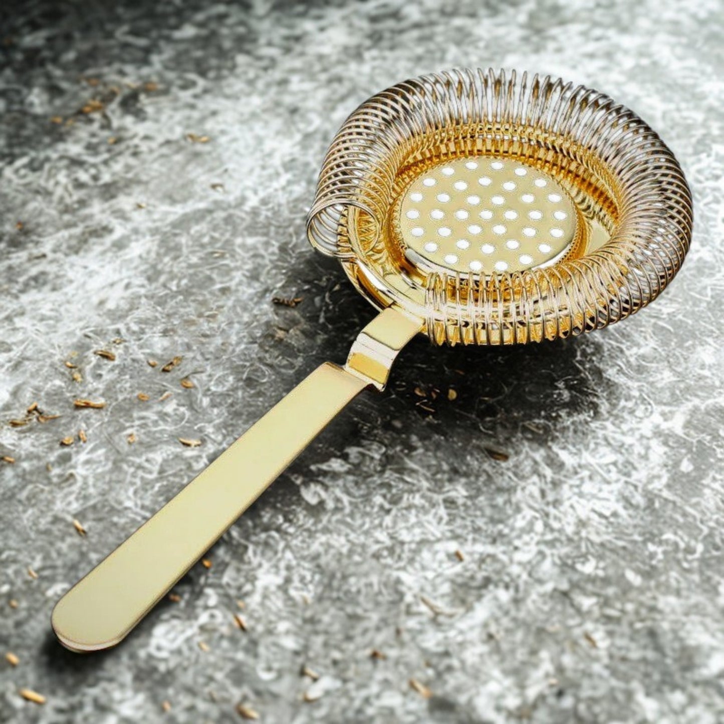 Gold cocktail strainer on a textured gray surface