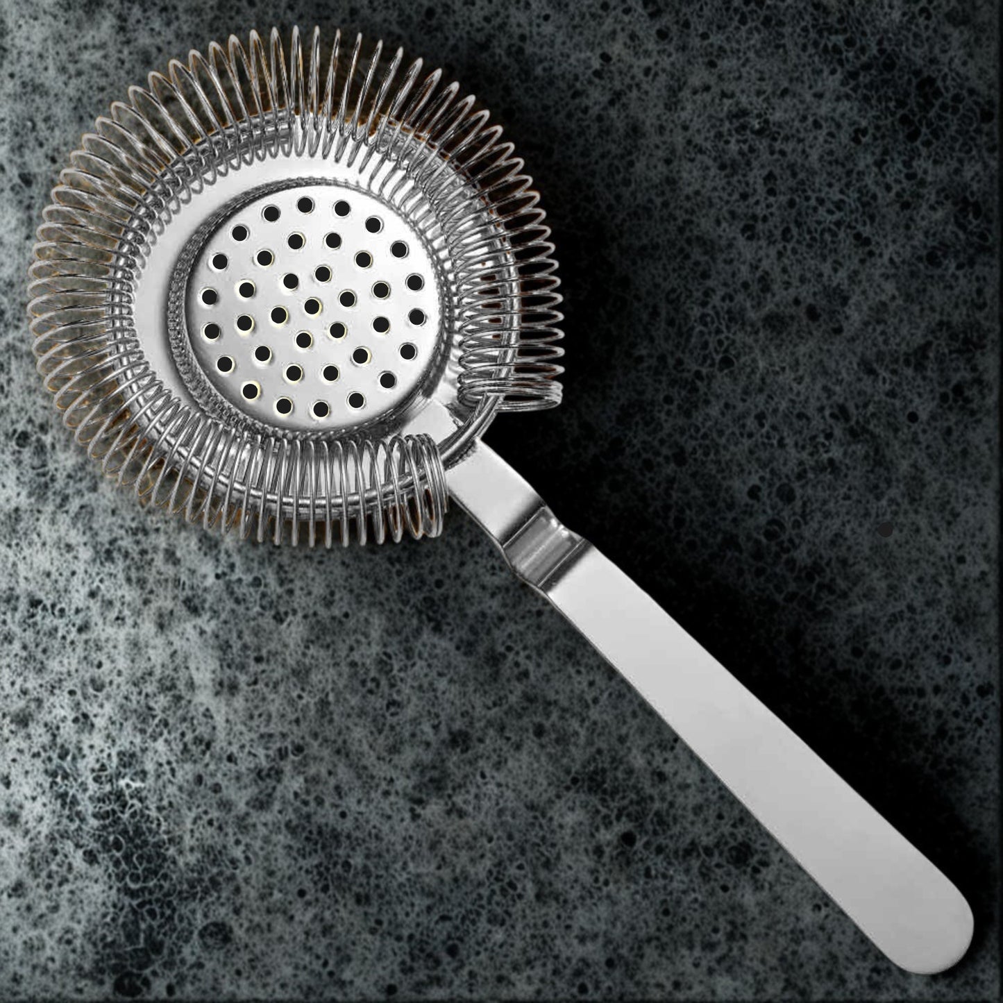Metallic cocktail strainer on a dark textured surface