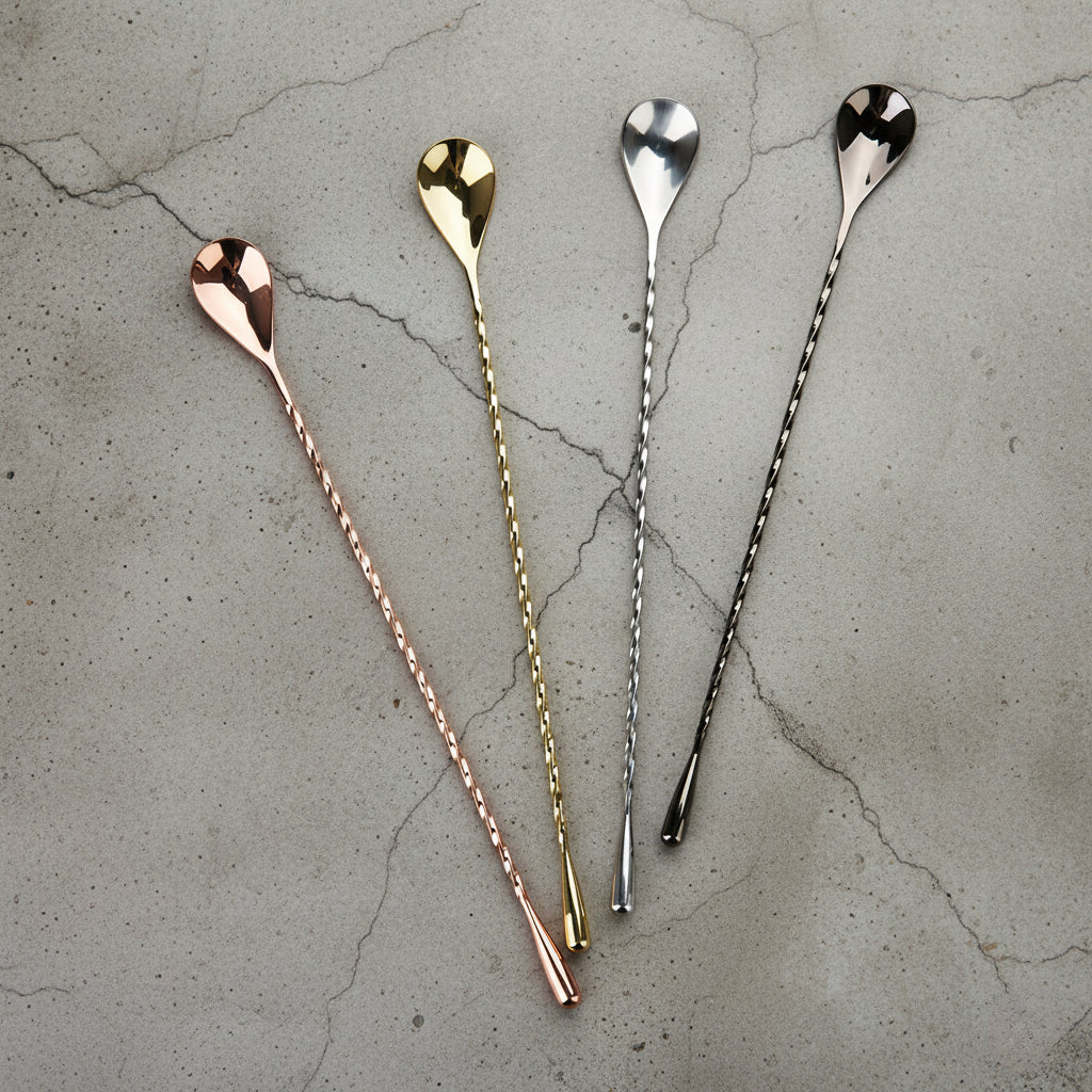 Four metallic spoons in rose gold, gold, silver, and black on a textured gray surface.