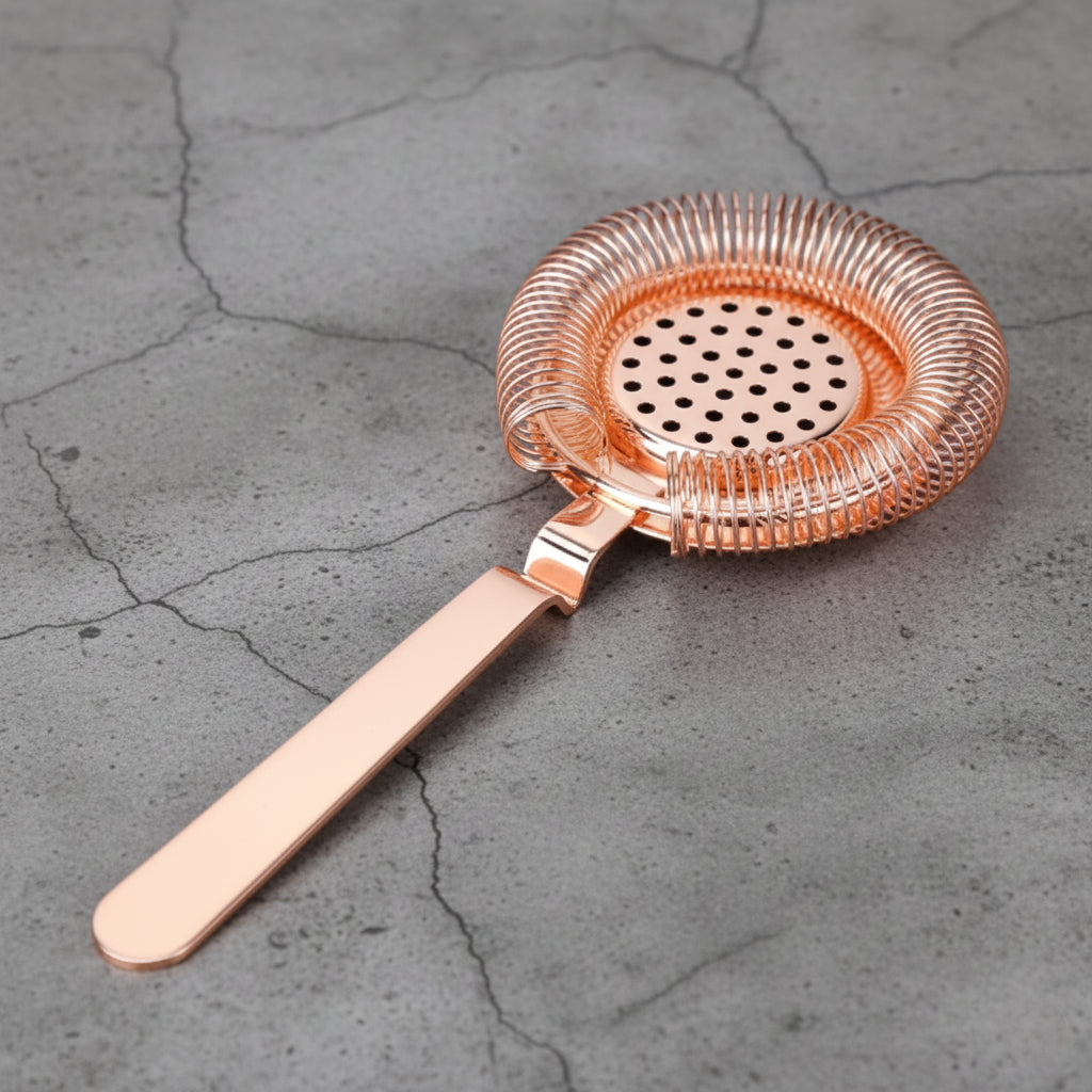 Rose gold cocktail strainer on a gray concrete surface
