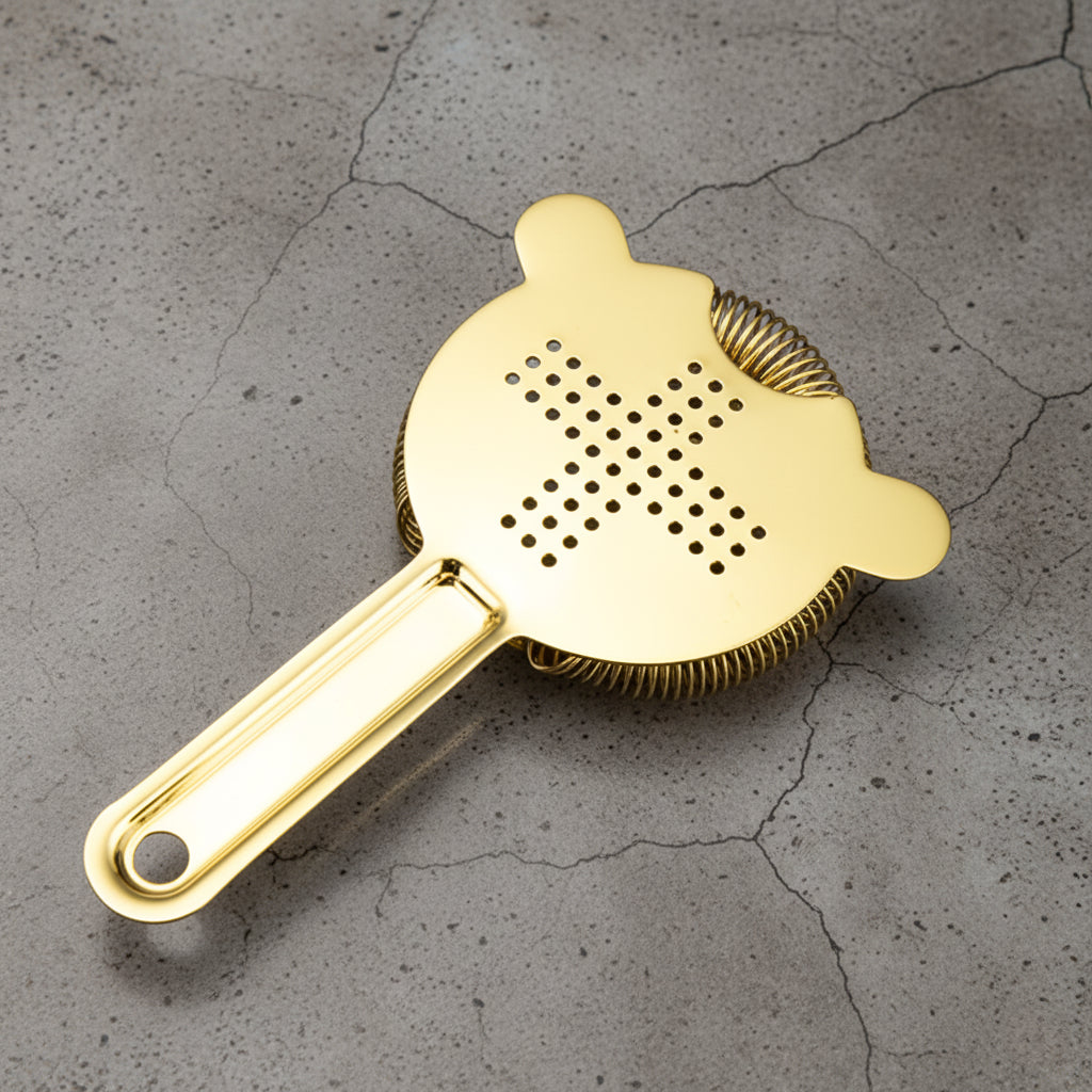 Gold cocktail strainer on a gray concrete surface