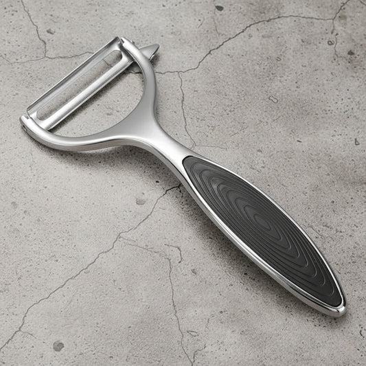 Silver vegetable peeler with black handle on a gray concrete surface