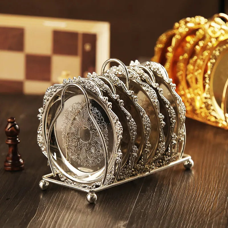Decorative silver coasters with intricate designs in a holder on a wooden surface.